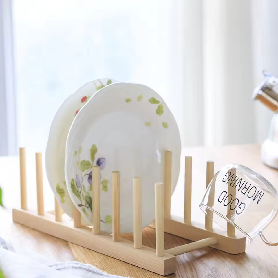 Wooden dish rack with plates and a glass on a light surface.